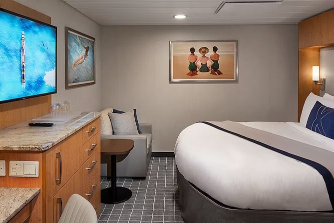 An Interior stateroom aboard Celebrity Xcel, king bed, sofa and desk with wood cabinetry An Interior stateroom aboard Celebrity Xcel, king bed, sofa and desk with wood cabinetry