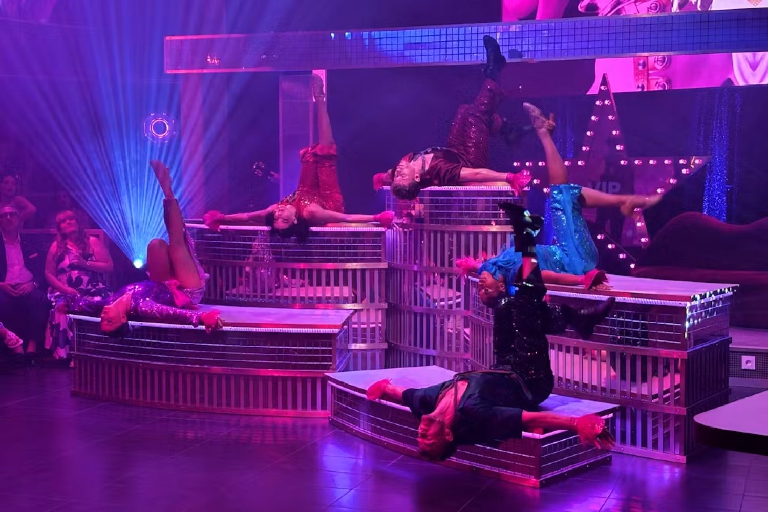 The Theatre in green light, the cast on the round stage against a rain-streaked New York skyline on the curved LED wall The Theatre in green light, the cast on the round stage against a rain-streaked New York skyline on the curved LED wall